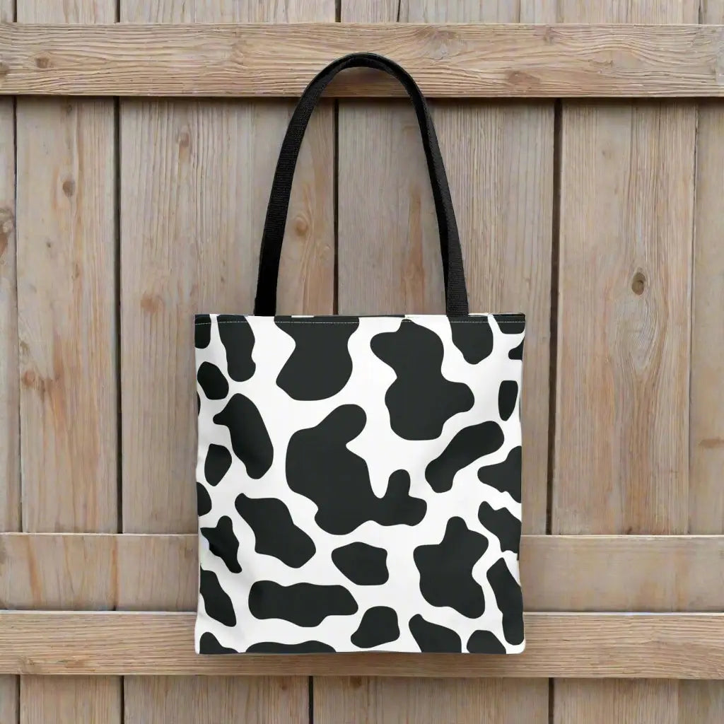 Black and white cow print tote bag with canvas material and black fabric handles for shopping and travel use